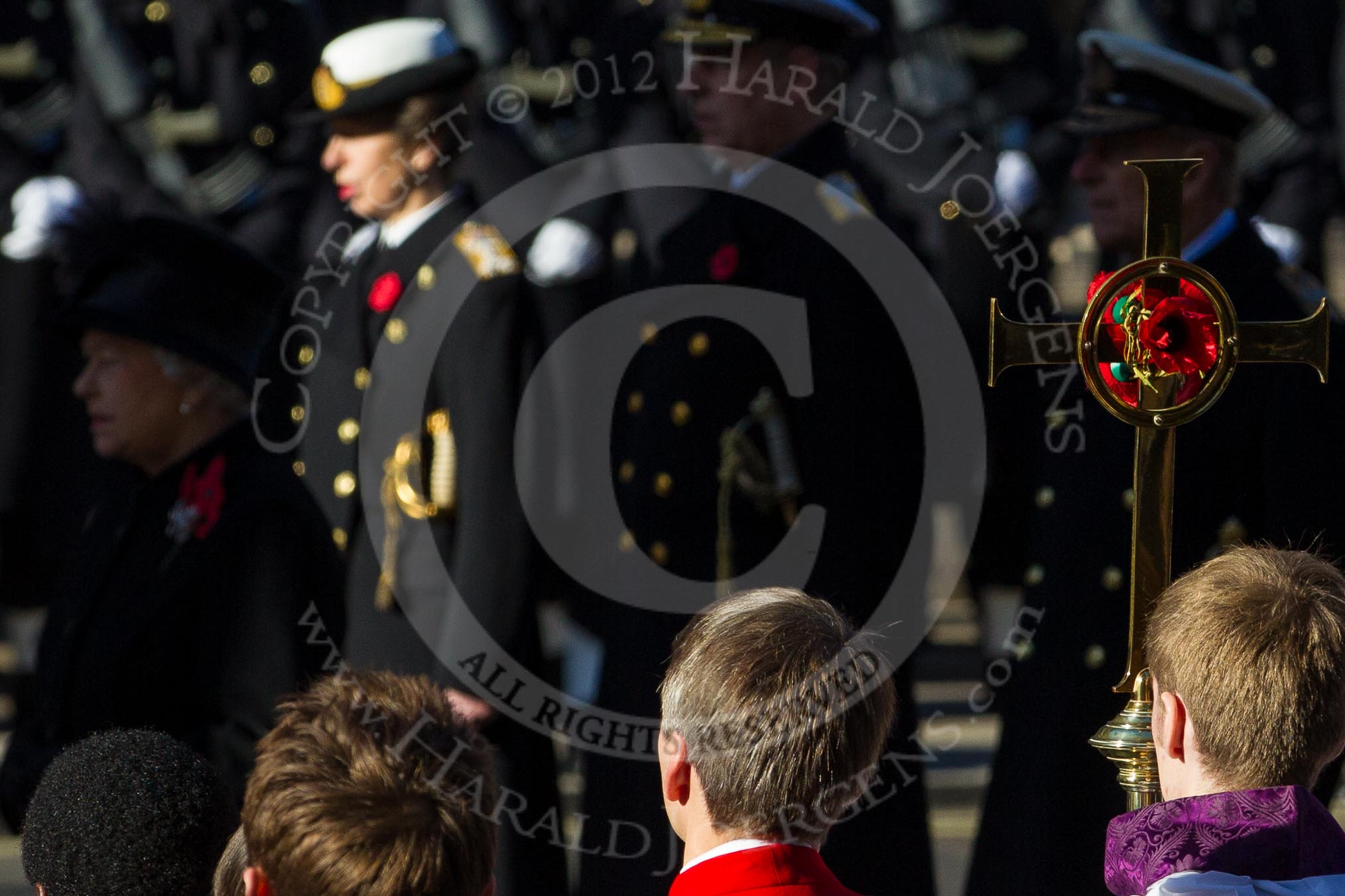 The choir boys and the golden cross with the red poppies, behind, and out of focus, HM The Queen and members of the Royal Family