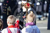HRH Prince Michael of Kent about to lay his wreath at the Cenotaph. He is out of focus behind the golden cross with the red poppies held by the cross bearer.