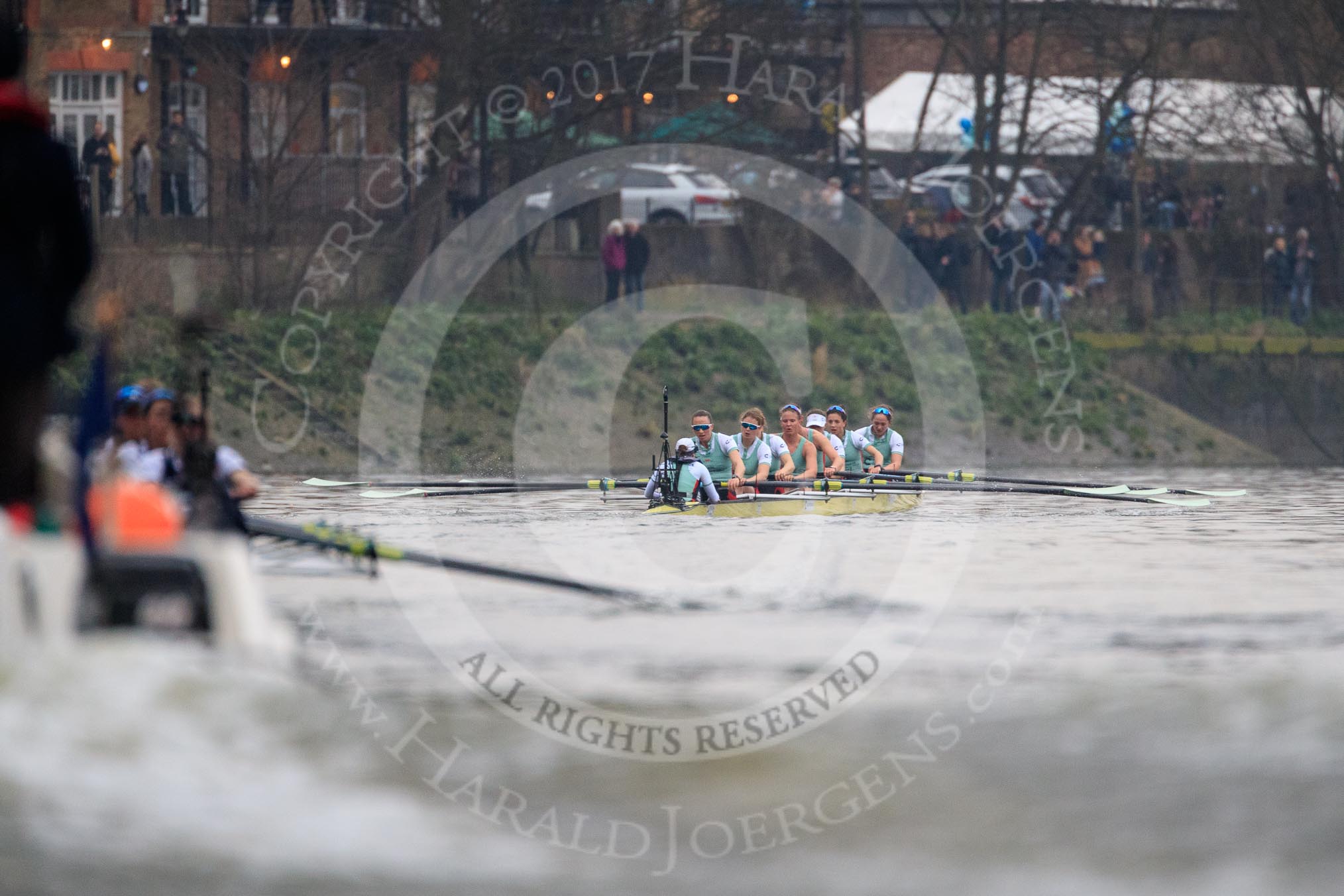The Cancer Research UK Women's Boat Race 2018: Near the White Hart pub in Barnes, the Oxford boat, on the left, is almost hidden behind the umpires's launch. In the leading Cambridge boat cox Sophie Shapter, stroke Olivia Coffey, 7 Myriam Goudet-Boukhatmi, 6 Alice White, 5 Paula Wesselmann, 4 Thea Zabell, 3 Kelsey Barolak, 2	Imogen Grant, bow Tricia Smith.
River Thames between Putney Bridge and Mortlake,
London SW15,

United Kingdom,
on 24 March 2018 at 16:47, image #199