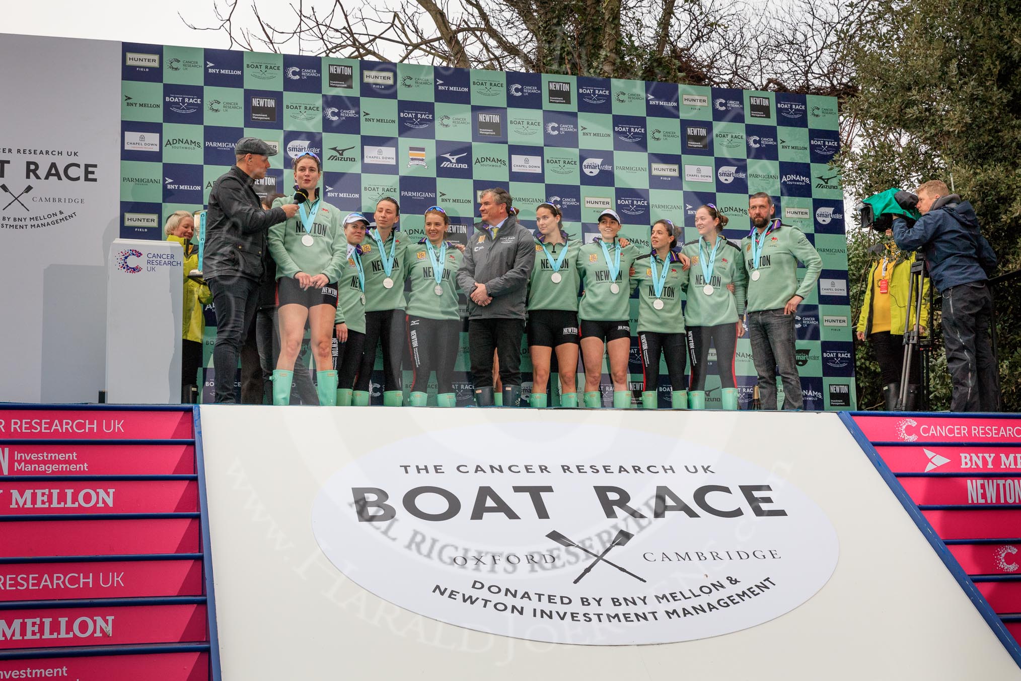 Photo 1803241708005SR9512HaraldJoergens The Cancer Research UK Women's Boat Race 2018: The Women's Boat race trophy presentation - BBC Sport commentator Jason Mohammad, Myriam Goudet-Boukhatmi, Sophie Shapter, Olivia Coffey, Alice White, Boat Race Company director Fergus Murison, behind him Paula Wesselmann, then Thea Zabell, Kelsey Barolak, Imogen Grant, Tricia Smith, and CUWBC Head Coach Rob Baker.
River Thames between Putney Bridge and Mortlake,
London SW15,
United Kingdom,
on 24 March 2018 at 17:07, image #268