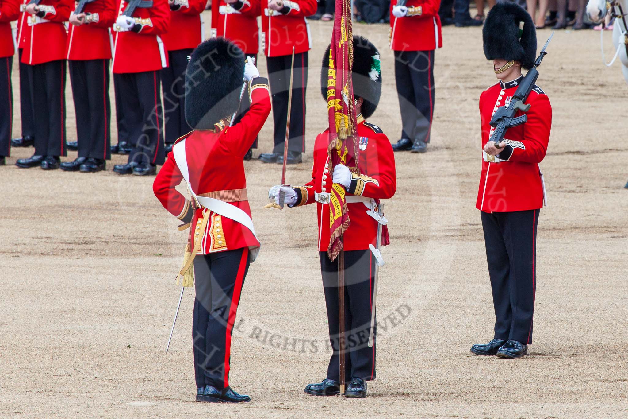 Trooping the Colour 2013: The Colour has been handed over from Colour Sergeant R J Heath, Welsh Guard to the Regimental Sergeant Major, WO1 Martin Topps, Welsh Guards. He now presents the Colour to the Ensign, Ensign, Second Lieutenant Joel Dinwiddle, who salutes the Colour with his sword. Image #453, 15 June 2013 11:21 Horse Guards Parade, London, UK