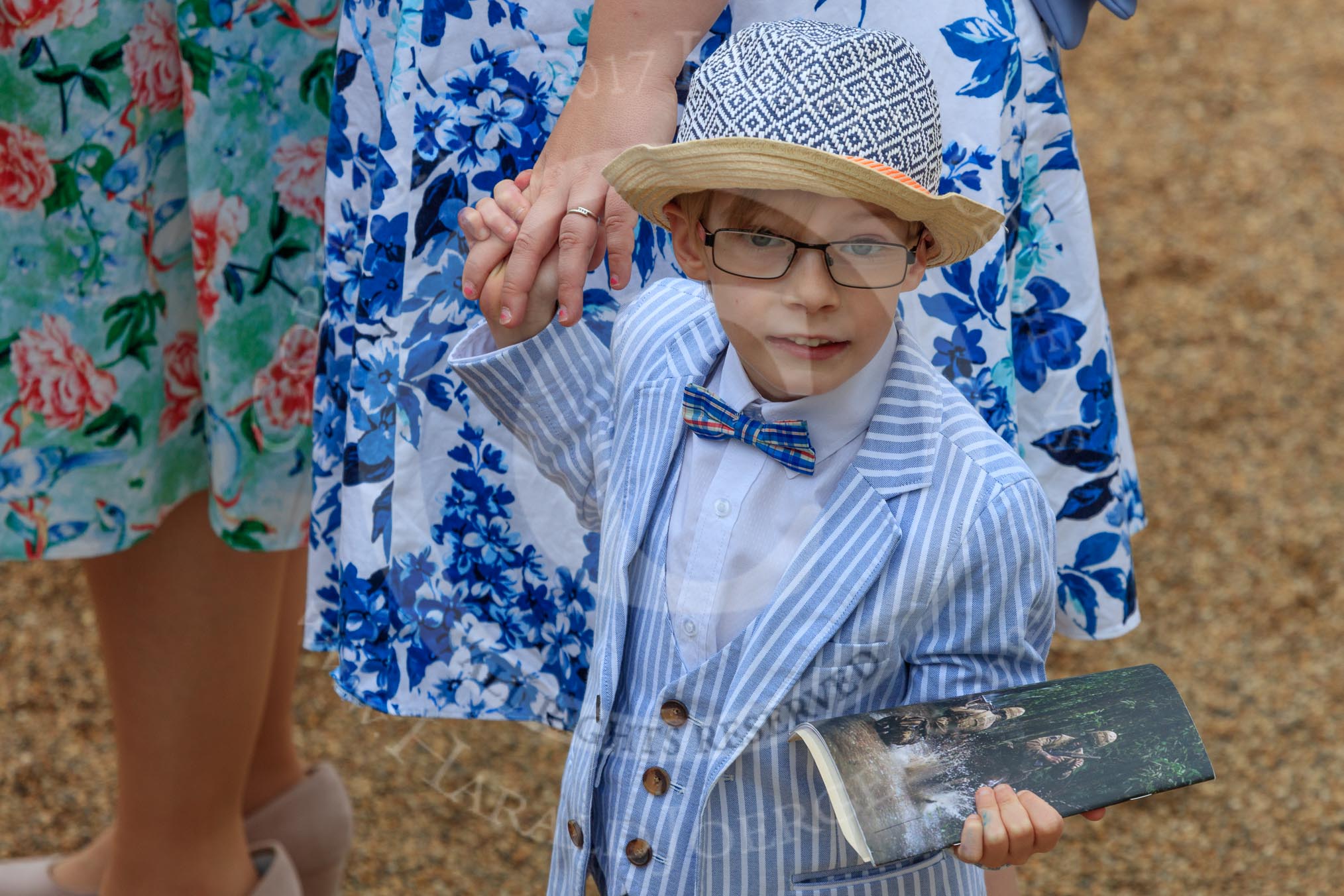 Young boy, wearing a striped three-piece-suit with a bow tie and a hat, holding a paper copy of the programme before The Colonel's Review 2018 (final rehearsal for Trooping the Colour, The Queen's Birthday Parade)  at Horse Guards Parade, Westminster, London, 2 June 2018, 09:13.