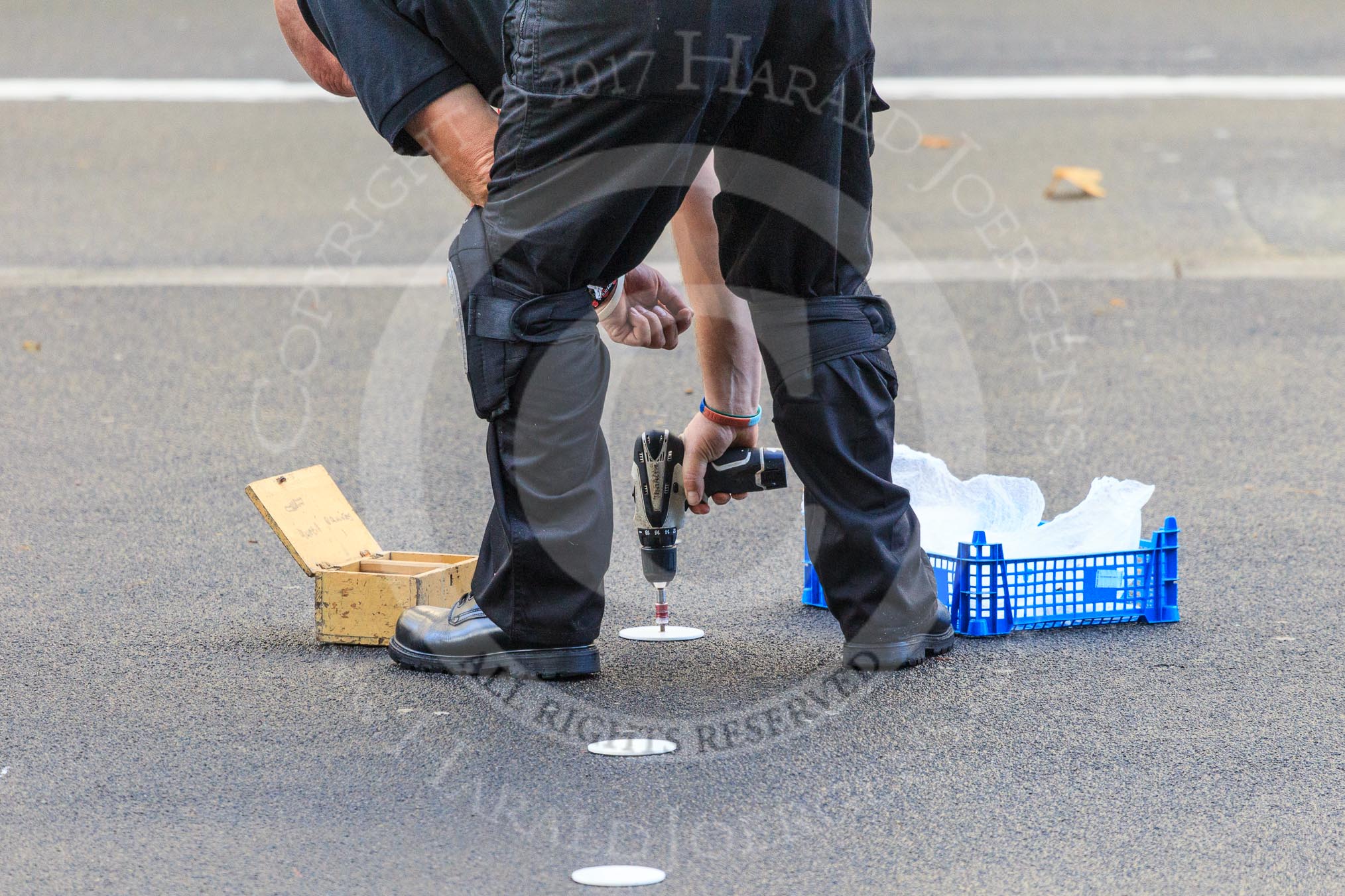 An Foreign and Commonwealth Office workman is screwing white discs onto the tarmac at Whitehall to mark the position of the members of the Royal Family and their Equerries before the  Remembrance Sunday Cenotaph Ceremony 2018 at Horse Guards Parade, Westminster, London, 11 November 2018, 08:54.