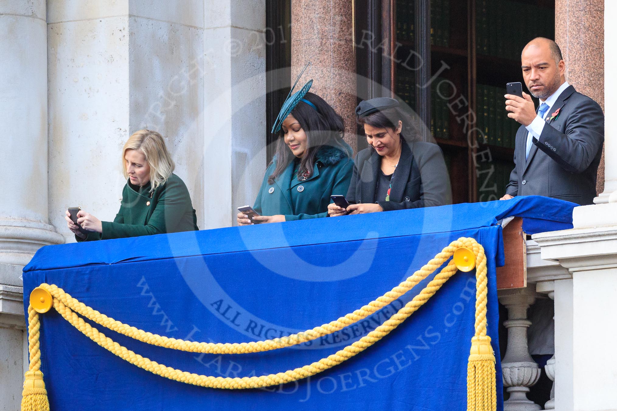 Early guests on one of the balconies of the Foreign and Commonwealth Office fiddling with their mobile phones before the Remembrance Sunday Cenotaph Ceremony 2018 at Horse Guards Parade, Westminster, London, 11 November 2018, 10:32.