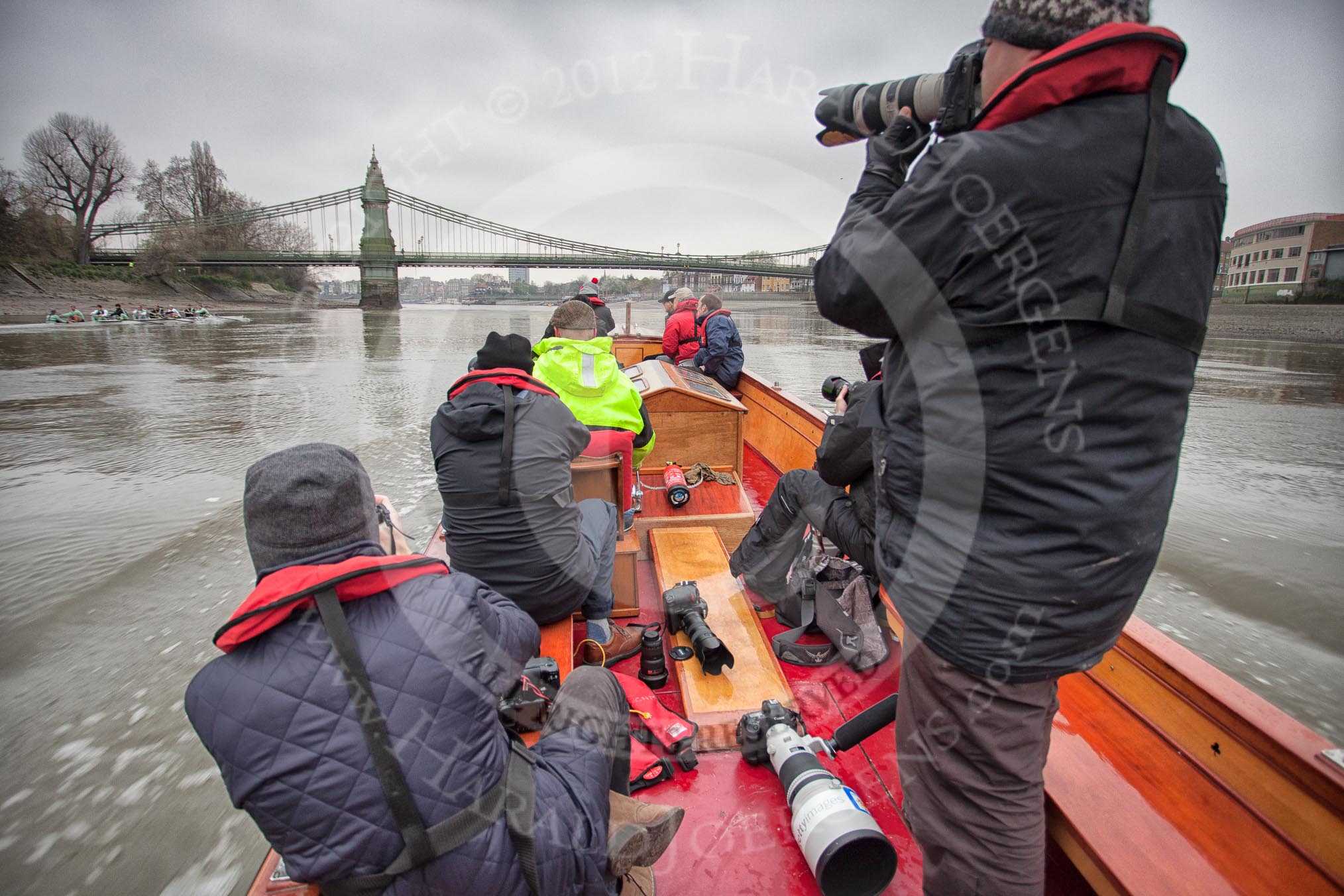 A press launch on the River Thames approaching Hammersmith Bridge, following the Cambridge University Boat Club Blue Boat.