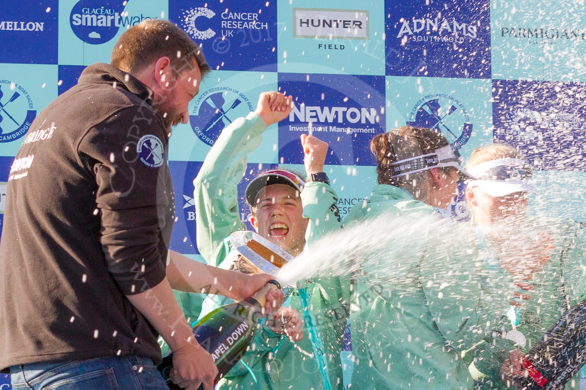 The Boat Race season 2017 -  The Cancer Research Women's Boat Race: CUWBC head coach Rob Barker spraying Champagne at the crew, on his right cox Matthew Holland.
River Thames between Putney Bridge and Mortlake,
London SW15,

United Kingdom,
on 02 April 2017 at 17:13, image #261