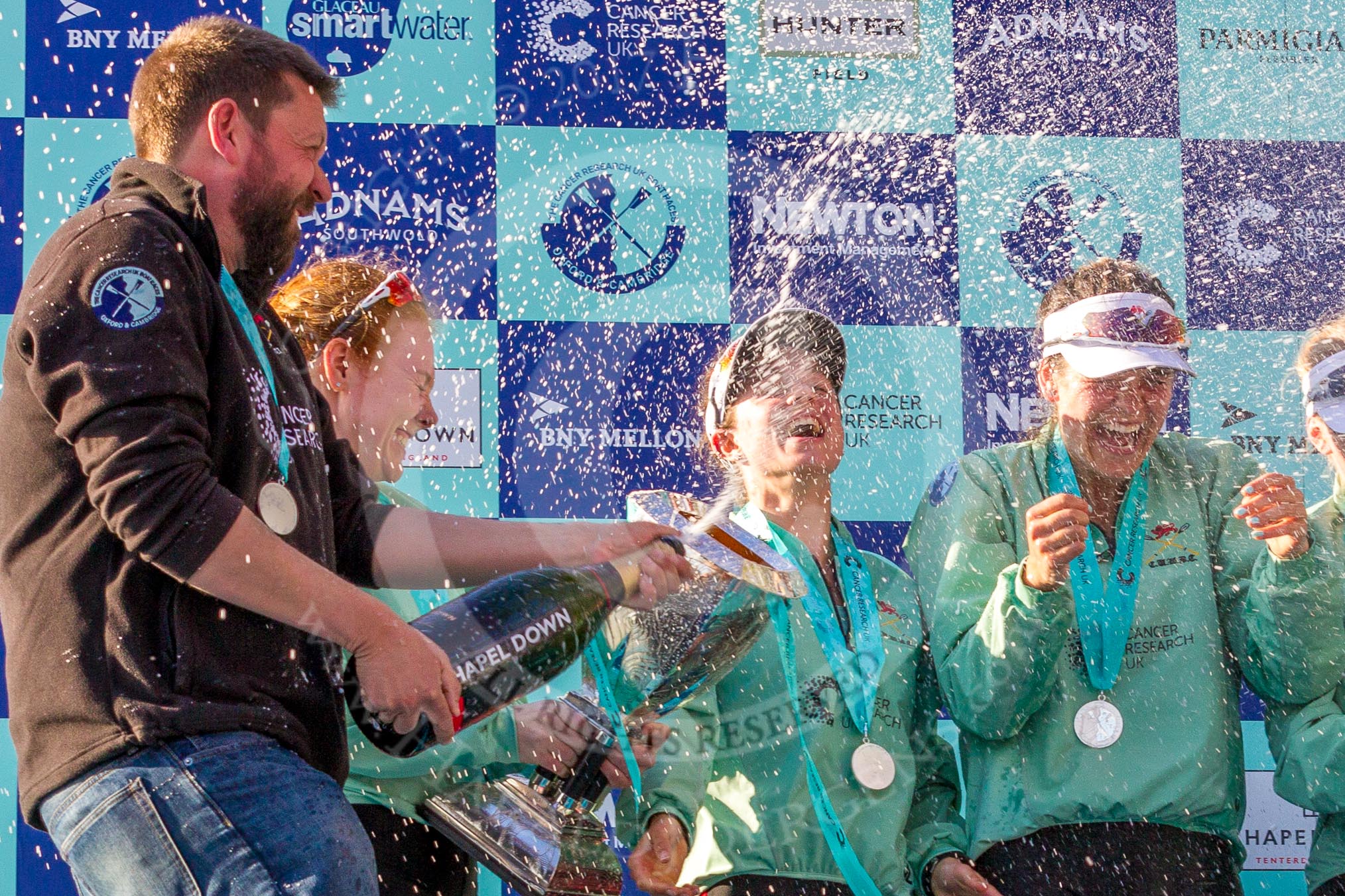 The Boat Race season 2017 -  The Cancer Research Women's Boat Race: CUWBC head coach Rob Barker spraying Champagne at the crew - here bow Ashton Brown, 2 Imogen Grant, and 3 Claire Lambe.
River Thames between Putney Bridge and Mortlake,
London SW15,

United Kingdom,
on 02 April 2017 at 17:13, image #271