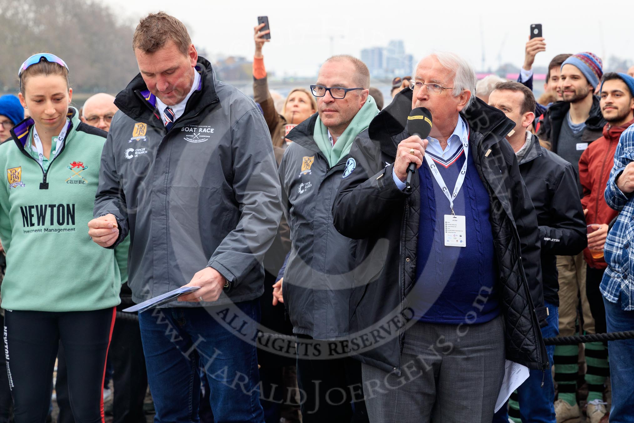 The Cancer Research UK Women's Boat Race 2018: Race umpire Sir Matthew Pinsent at the toss. On the left Cambridge stroke Olivia Coffey, and , with the microphone, for the BBC sports broadcaster David Mercer.
River Thames between Putney Bridge and Mortlake,
London SW15,

United Kingdom,
on 24 March 2018 at 14:40, image #34