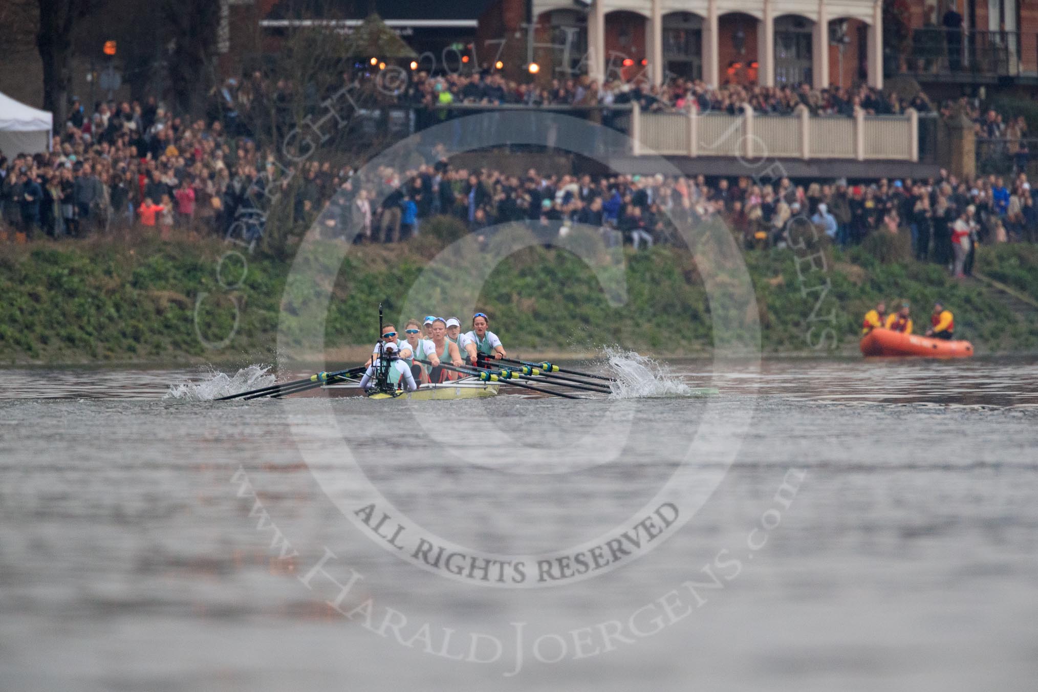 The Cancer Research UK Women's Boat Race 2018: The Cambridge boat passing the packed White Hart pub in Barnes - cox Sophie Shapter, stroke Olivia Coffey, 7 Myriam Goudet-Boukhatmi, 6 Alice White, 5 Paula Wesselmann, 4 Thea Zabell, 3 Kelsey Barolak, 2	Imogen Grant, bow Tricia Smith.
River Thames between Putney Bridge and Mortlake,
London SW15,

United Kingdom,
on 24 March 2018 at 16:47, image #198
