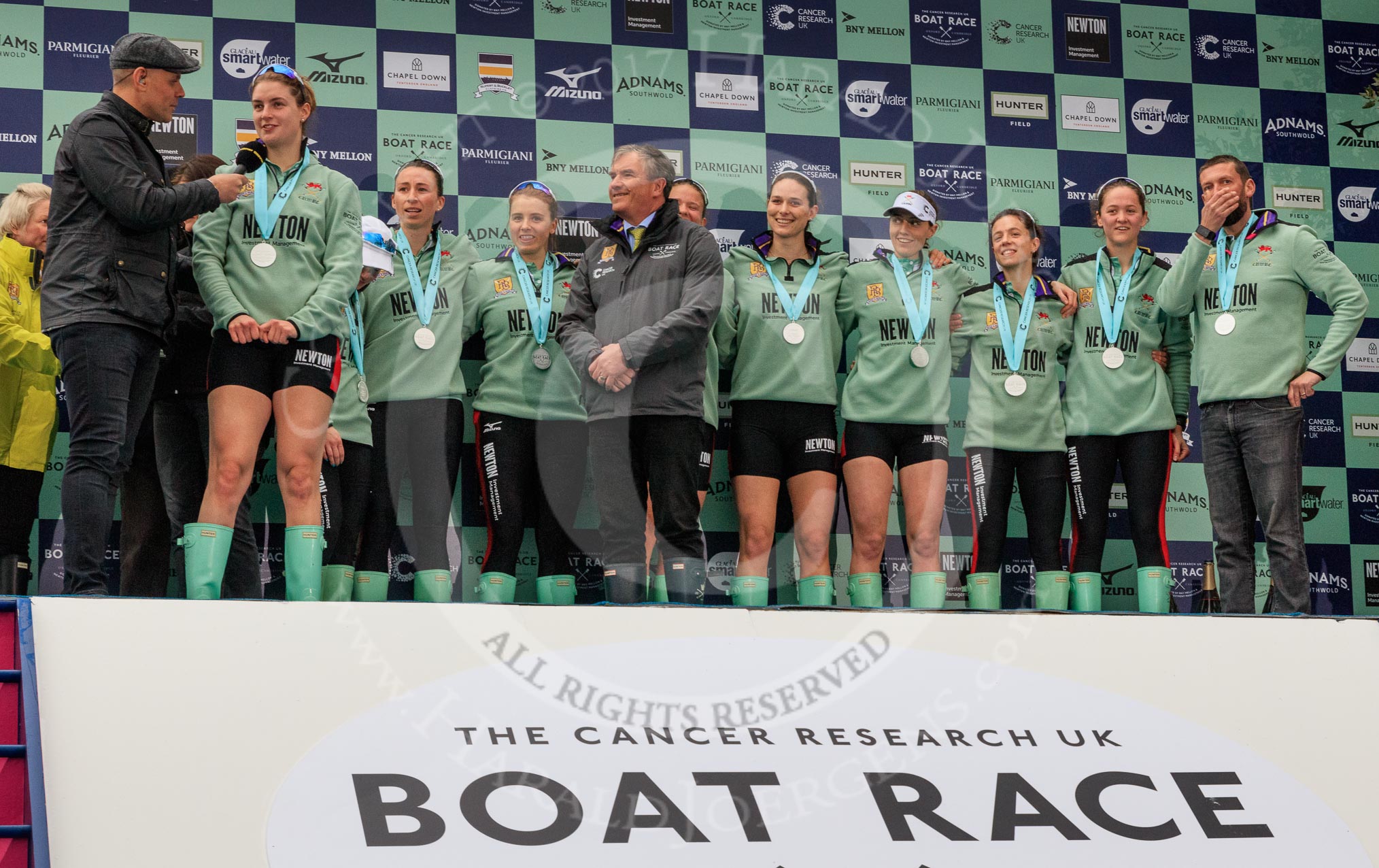 The Cancer Research UK Women's Boat Race 2018: The Women's Boat race trophy presentation - BBC Sport commentator Jason Mohammad, Myriam Goudet-Boukhatmi, Sophie Shapter, Olivia Coffey, Alice White, Boat Race Company director Fergus Murison, behind him Paula Wesselmann, then Thea Zabell, Kelsey Barolak, Imogen Grant, Tricia Smith, and CUWBC Head Coach Rob Baker.
River Thames between Putney Bridge and Mortlake,
London SW15,

United Kingdom,
on 24 March 2018 at 17:08, image #269