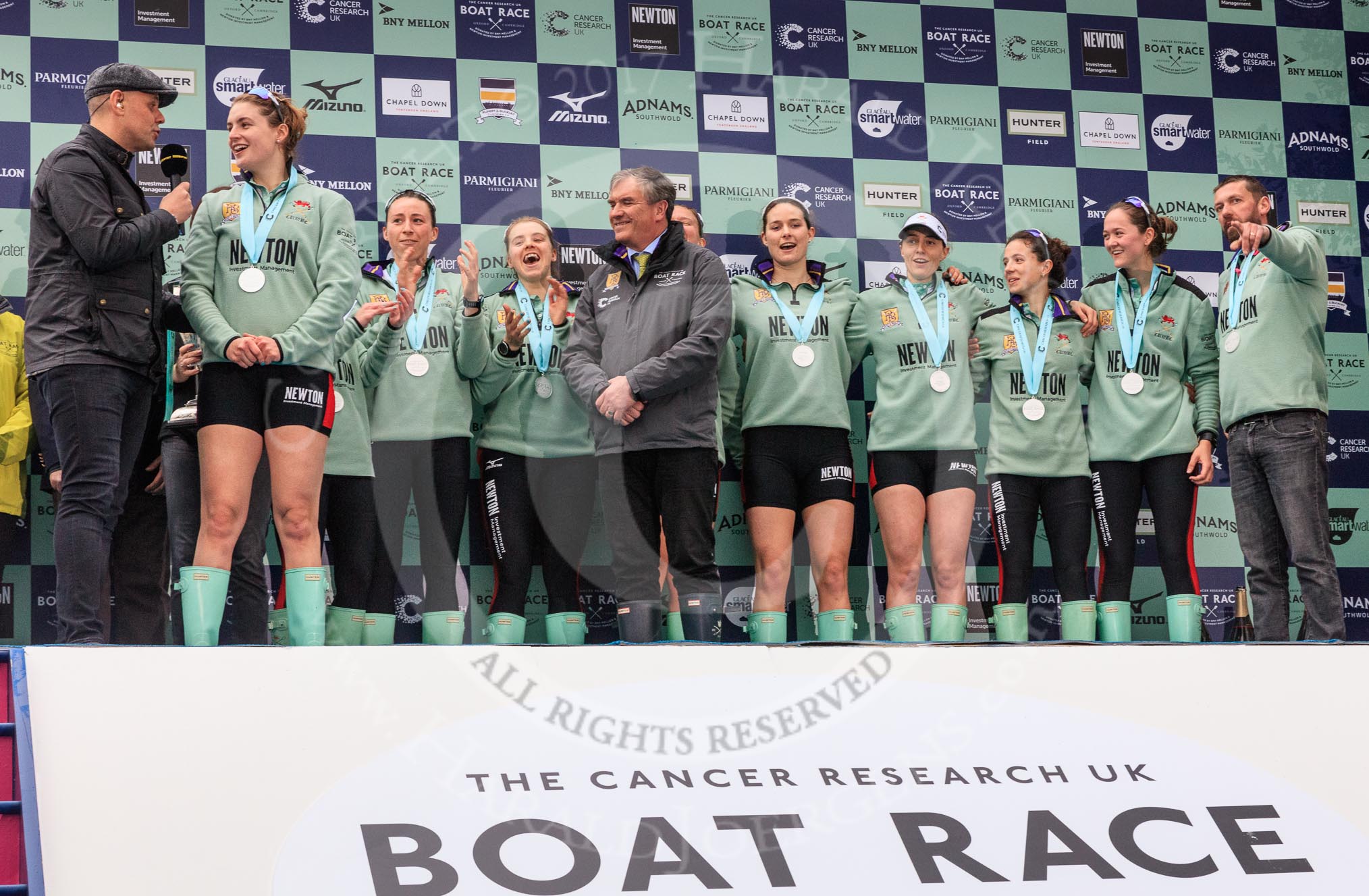 The Cancer Research UK Women's Boat Race 2018: The Women's Boat race trophy presentation - BBC Sport commentator Jason Mohammad, Myriam Goudet-Boukhatmi, Sophie Shapter, Olivia Coffey, Alice White, Boat Race Company director Fergus Murison, behind him Paula Wesselmann, then Thea Zabell, Kelsey Barolak, Imogen Grant, Tricia Smith, and CUWBC Head Coach Rob Baker.
River Thames between Putney Bridge and Mortlake,
London SW15,

United Kingdom,
on 24 March 2018 at 17:08, image #270
